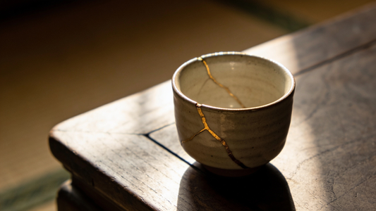 Reparierte Keramiktasse mit goldenen Nähten im Kintsugi-Stil auf dunklem Holztisch; KI-gestützt erstellt